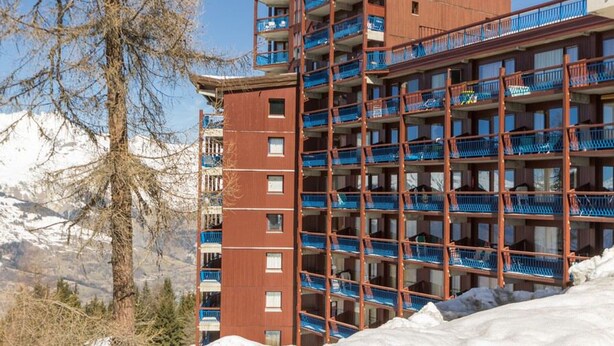 Un hôtel à plusieurs étages doté de balcons, entouré de montagnes enneigées.