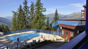 Un espace piscine doté d’une terrasse en bois, de chaises longues et offrant une vue sur les montagnes.
