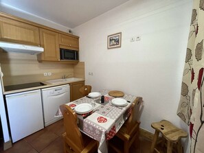 Uma cozinha compacta com armários de madeira, micro-ondas, pia e mesa de jantar para quatro pessoas.