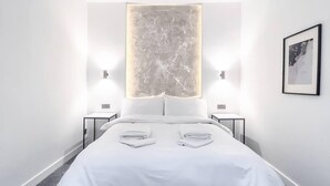 Una habitación de hotel moderna con una cama grande, dos mesitas de noche y una lámpara fijada a la pared.