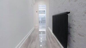 Un pasillo con un radiador, una puerta blanca y un baño a lo lejos.