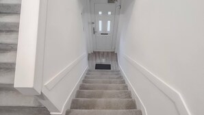 Una escalera con peldaños alfombrados que conduce a una puerta blanca con una pequeña rejilla encima.