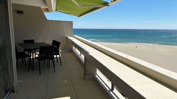Un balcon avec une table et des chaises, donnant sur une plage et l’océan.