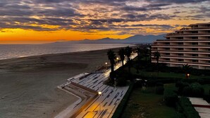 Un hôtel situé en bord de mer, offrant une vue sur l’océan et les montagnes au coucher du soleil.