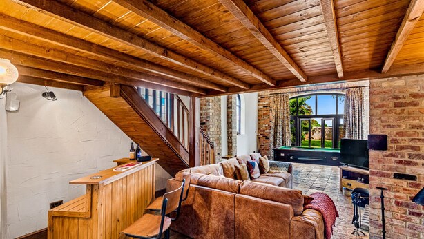A cozy living area with a wooden ceiling, a brick wall, a sofa, a TV, and a pool table. - Church Walk Farm (Snarestone)