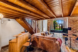 A cozy living area with a wooden ceiling, a brick wall, a sofa, a TV, and a pool table. - Church Walk Farm (Snarestone)
