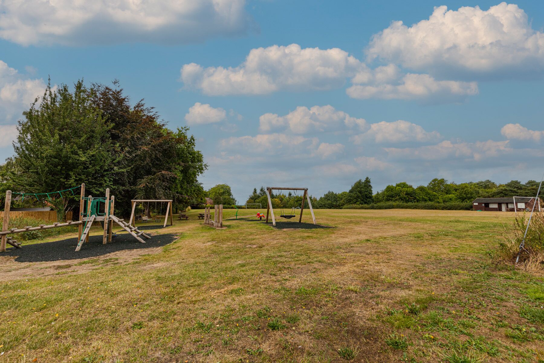 A playground with swings and a climbing structure in a grassy field.