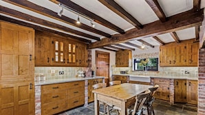 A rustic kitchen with wooden cabinets, a stone-tiled floor, and exposed wooden beams on the ceiling. - Church Walk Farm (Snarestone)