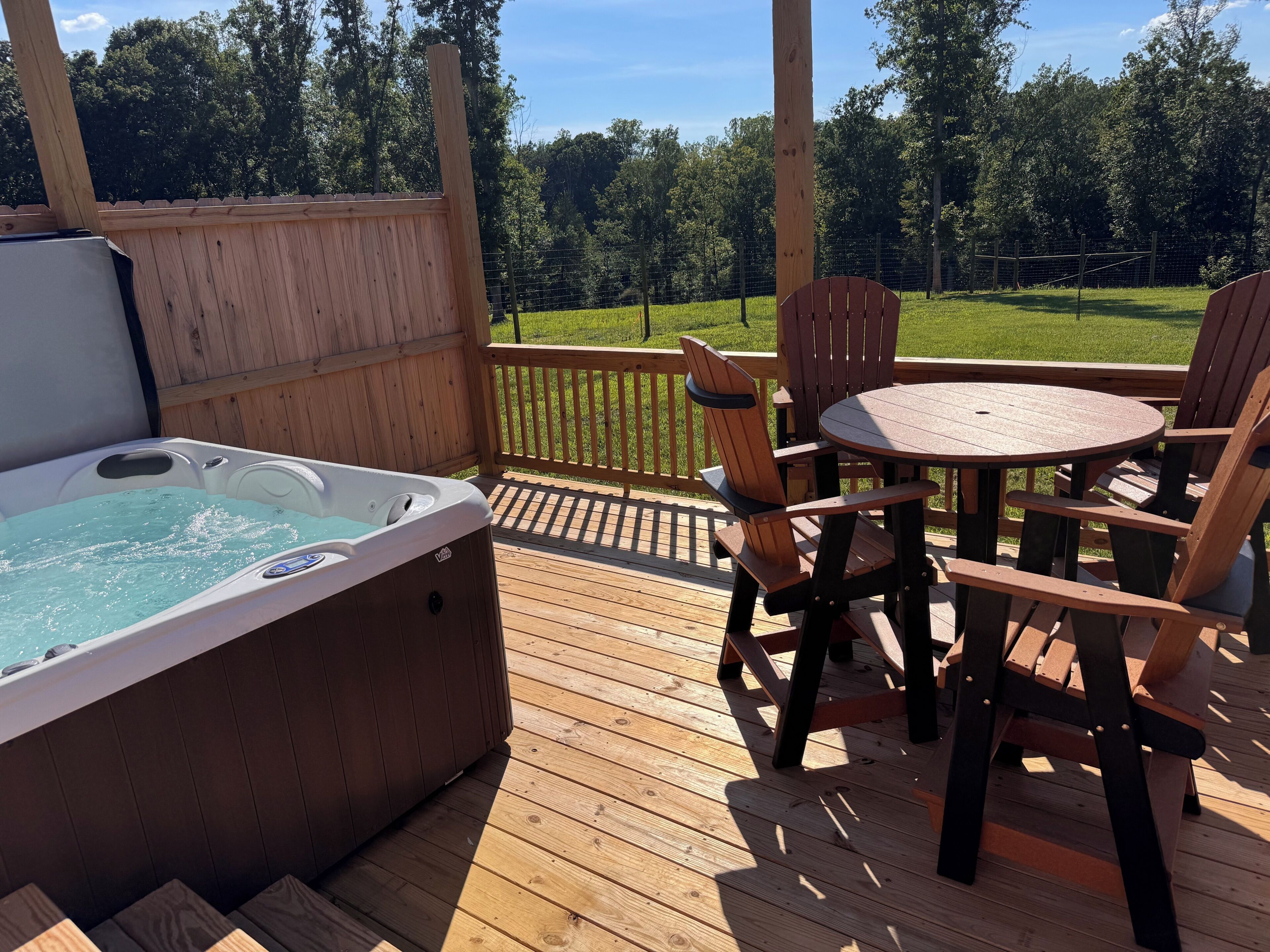 A wooden deck with a hot tub, wooden chairs, and a table.