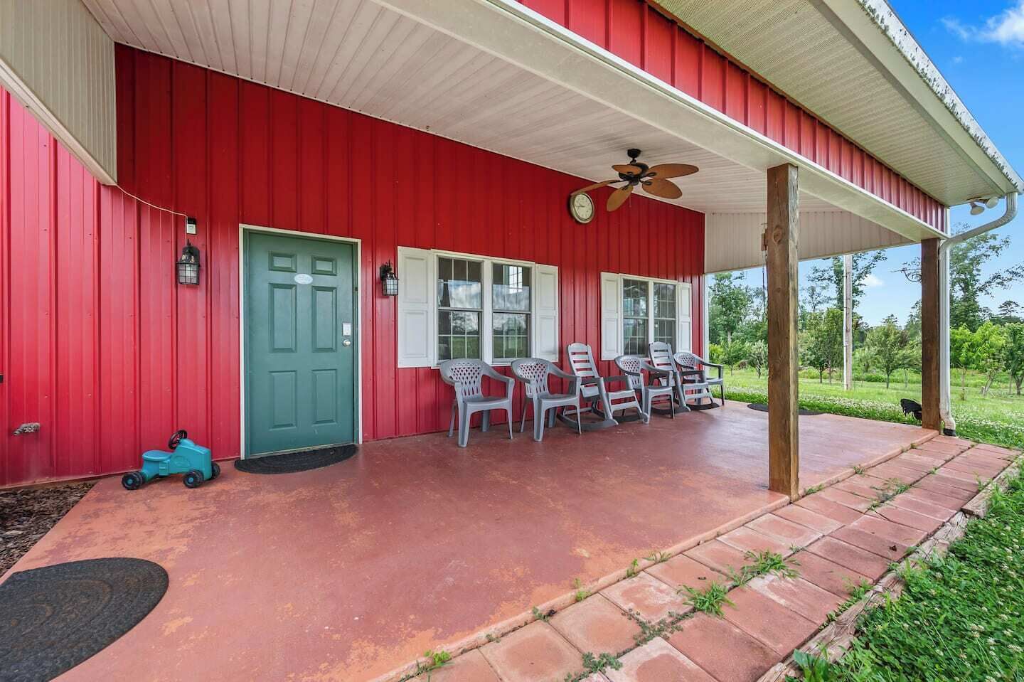 A red building with a covered porch, a green door, and several chairs.