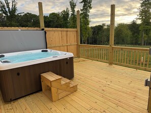Un bain à remous sur une terrasse en bois, avec vue sur les arbres et un ciel nuageux.