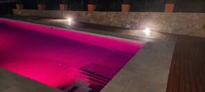 A swimming pool with a pink interior, surrounded by a stone wall and wooden deck.