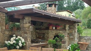 An outdoor patio with stone flooring, wooden tables and chairs, and a stone fireplace. - Fantastic farmhouse with swimming pool just a step away from Cinque Terre. (Sesta Godano)