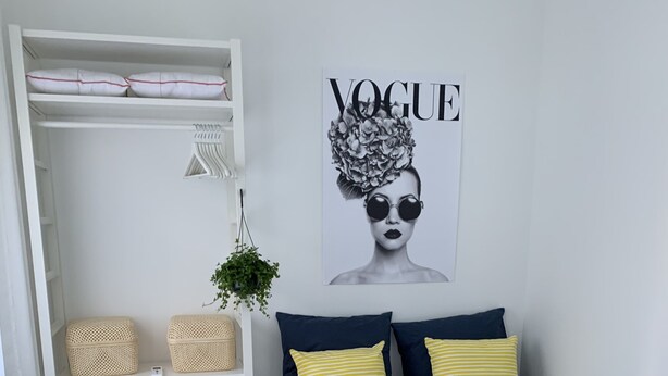 A bedroom with a bed, a white wardrobe, a hanging plant, and a 'Vogue' poster on the wall.