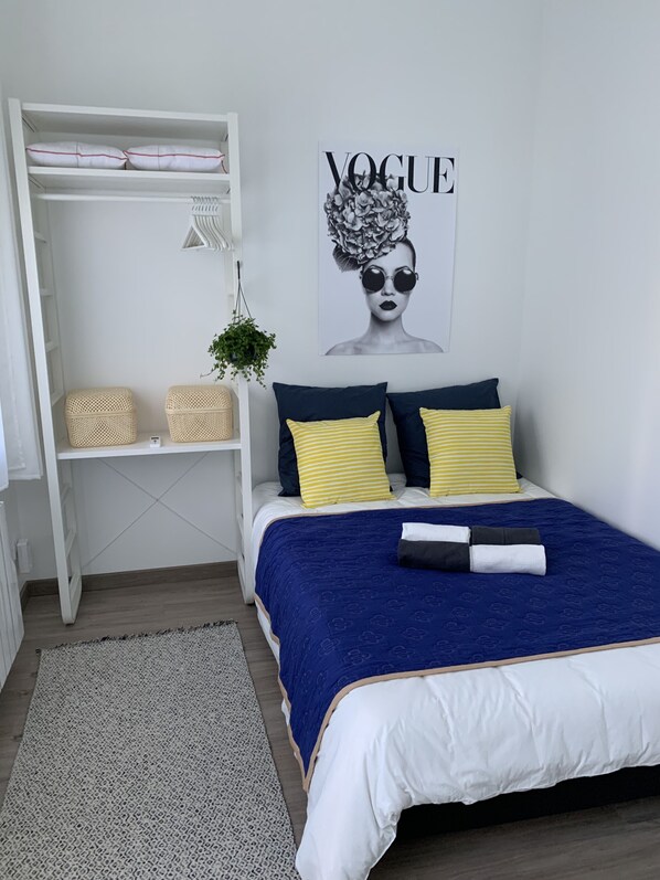 Um quarto com uma cama, um guarda-roupa branco, uma planta pendente e um cartaz da 'Vogue' na parede.