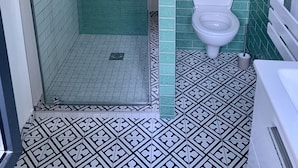 A bathroom with a shower, toilet, and patterned floor tiles.