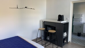 A compact hotel room with a bed, a kitchenette, and a city skyline decal on the wall.