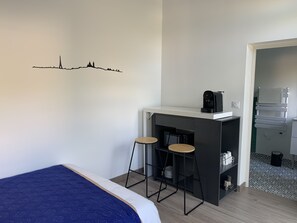 Quarto de hotel compacto com cama, cozinha compacta e decalque de horizonte urbano na parede.