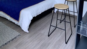 A bedroom with a bed, two stools, a small table, and a wall art piece.
