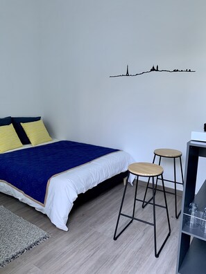 Quarto com uma cama, dois banquinhos, uma mesinha e uma obra de arte na parede.