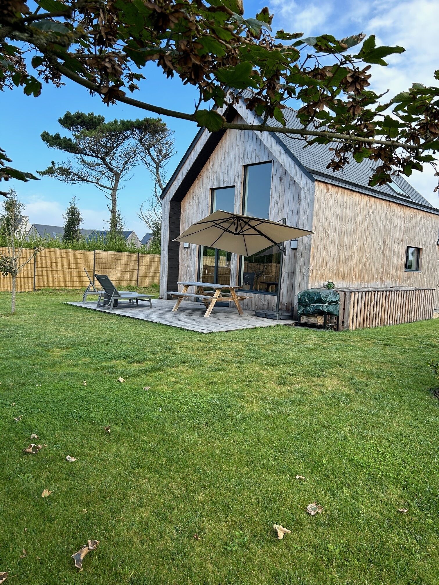 Ein modernes Haus mit Holzfassade, einer Terrasse mit Tisch und Stühlen sowie einem großen Sonnenschirm.