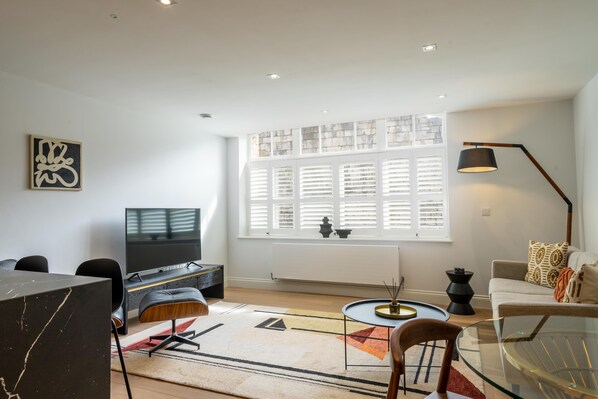 A modern living room with a large window, a flat-screen TV, a glass coffee table, and a sofa. - A premium stay that sleeps 4 guests in 2 bedrooms (York)