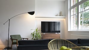 Ett modernt vardagsrum med en svart soffa, en grön fåtölj, en golvlampa, en tv och ett stort fönster.