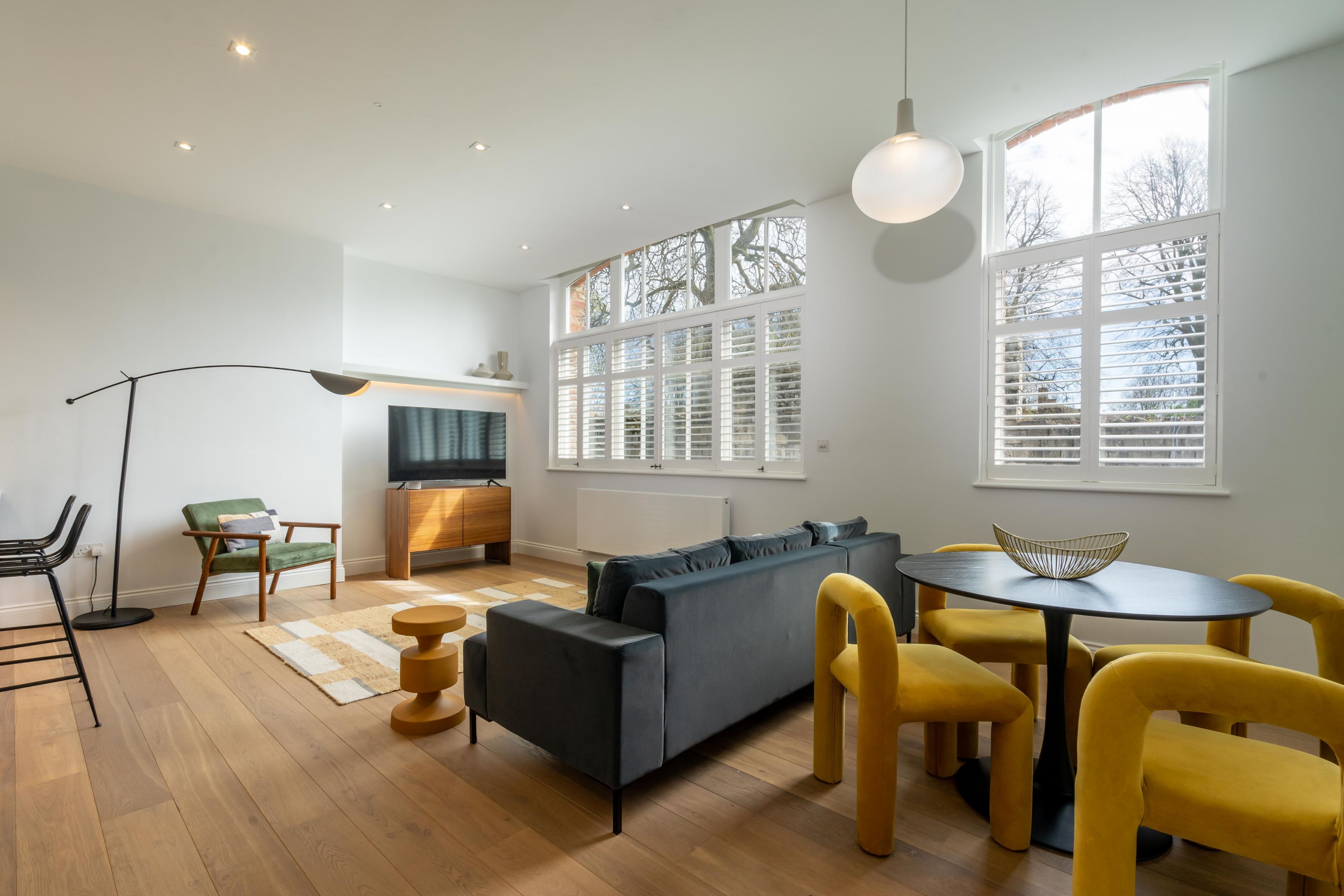 Ein modernes Wohnzimmer mit einem grauen Sofa, gelben Sesseln, einem runden Tisch und einem Fernseher.