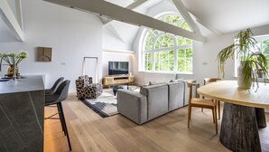 Een ruime woonkamer met een groot raam, een moderne bank, een eettafel en een keukenhoek.