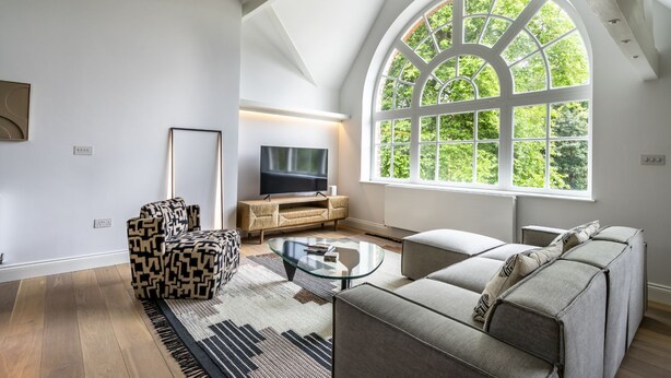 Een ruime woonkamer met een groot rondboogvenster, een flatscreen televisie, een gestreept bankstel en een glazen salontafel.