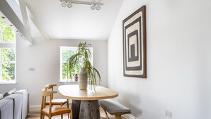 Een eetgedeelte met een ronde houten tafel, twee stoelen, een bankje en een potplant.