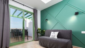 Ein modernes Wohnzimmer mit einer Schiebeglastür, die auf einen Balkon führt, einem grauen Sofa mit Kissen und einer grünen Akzentwand.