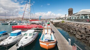 Ein Yachthafen mit verschiedenen angestaubten Booten, darunter ein markantes rotes Boot mit der Aufschrift "Obycat.com", und ein historischer Turm im Hintergrund.