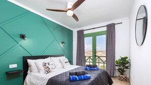 Ein modernes Schlafzimmer mit einem Bett, einem Deckenventilator, einem Fenster mit Vorhängen und einer Topfpflanze.