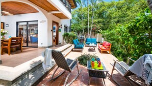 Une terrasse aménagée avec du mobilier d’extérieur, un coin repas et une vue sur une végétation luxuriante et des palmiers.