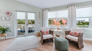 A spacious room with two wicker chairs, a small round table, a green ottoman, and a patterned rug.