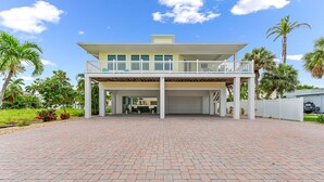 A two-story house with a covered patio, a garage, and a well-maintained garden with palm trees and flowering plants.