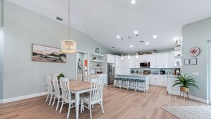 A modern kitchen with white cabinets, a dining area with white chairs, and a central island.