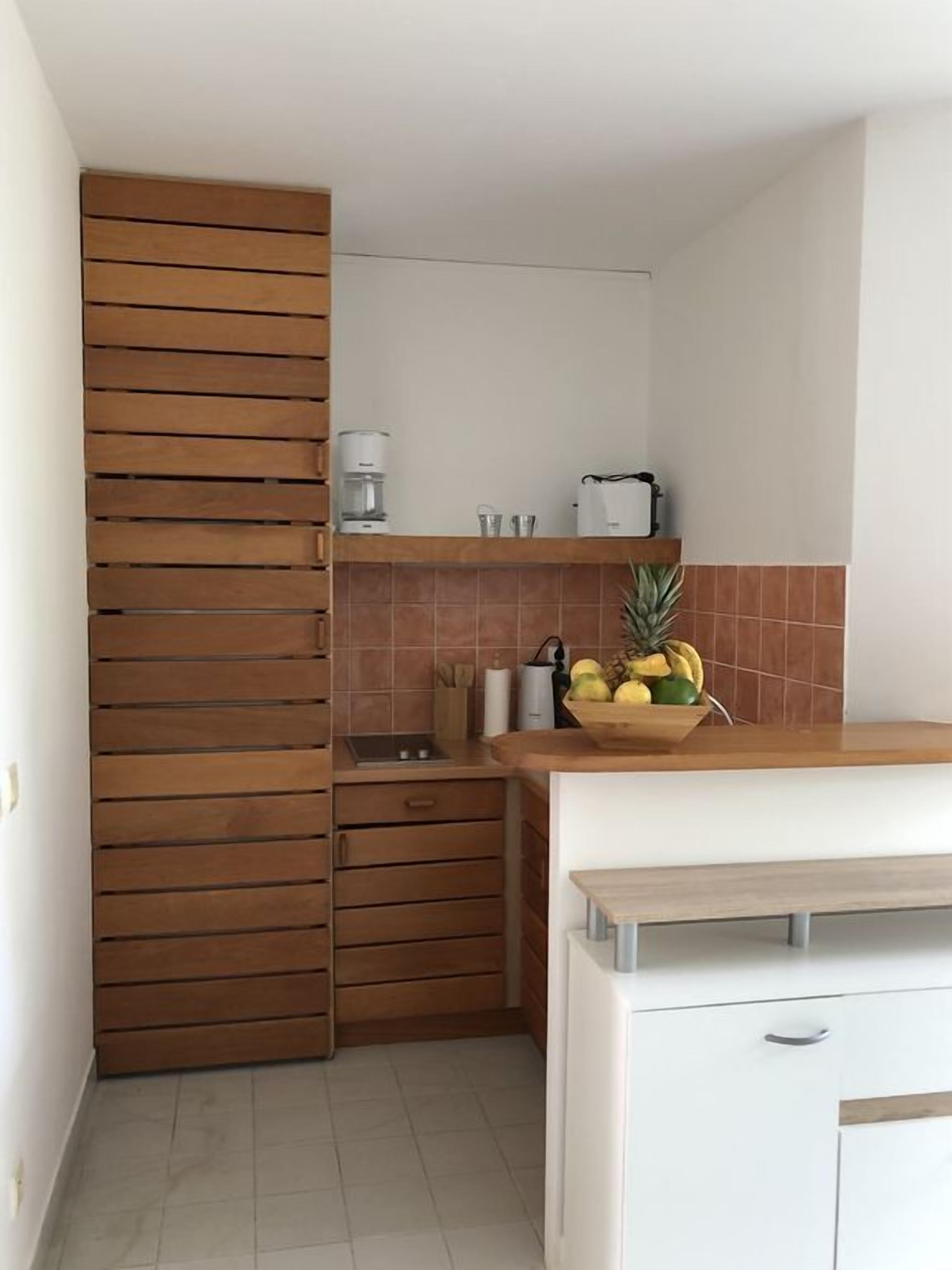 A compact kitchen with a wooden cabinet, a countertop with a fruit bowl, and a coffee maker.