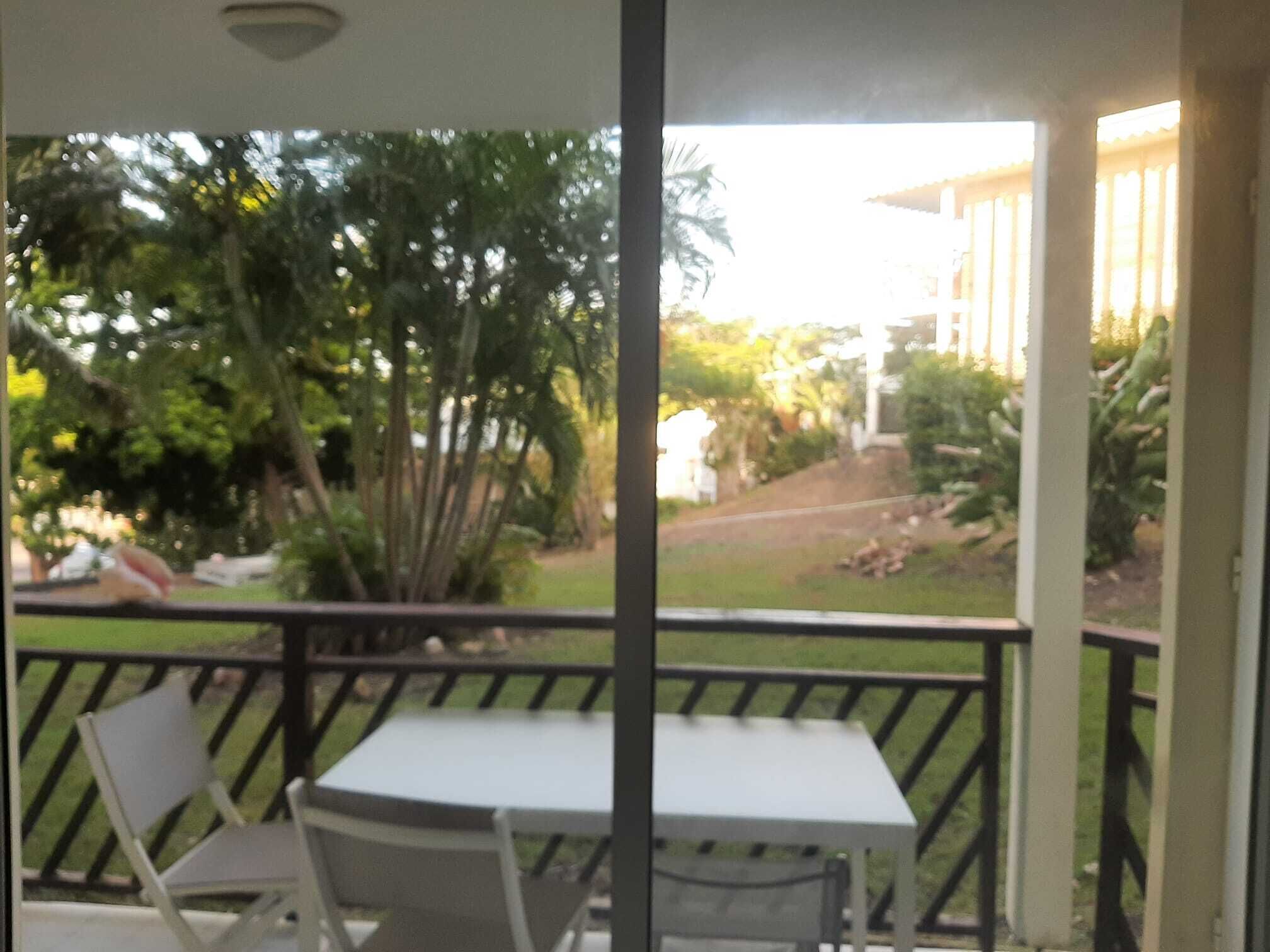 Un balcon avec une table et des chaises, donnant sur un jardin arboré et sur un bâtiment situé au loin.