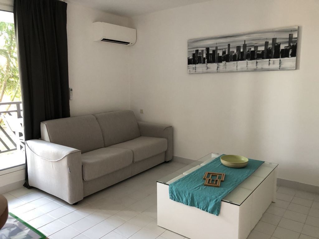 A modern living room with a beige sofa, a white coffee table with a teal cloth, and a cityscape painting on the wall.