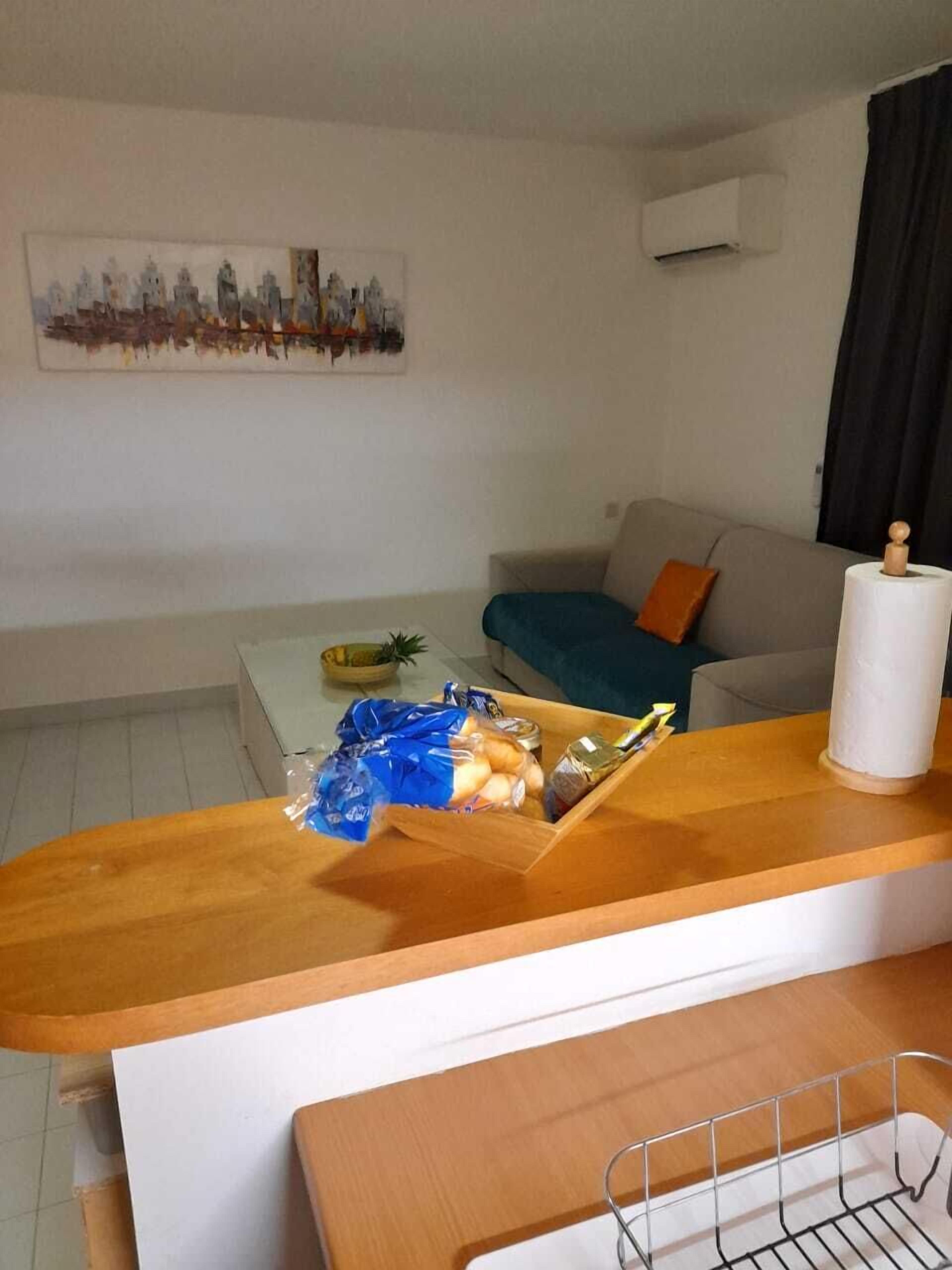 A living room with a wooden coffee table, a blue cushion on a sofa, and a painting on the wall.
