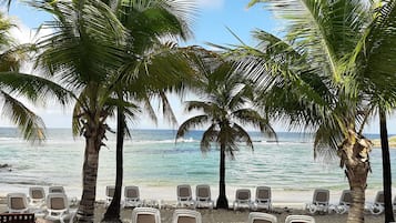 Di pantai, pasir putih, kursi berjemur, dan payung pantai