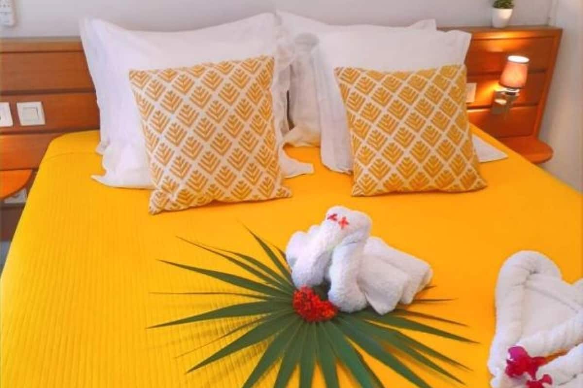 A bed with yellow bedding, two patterned pillows, and a decorative arrangement of towels and a palm leaf.
