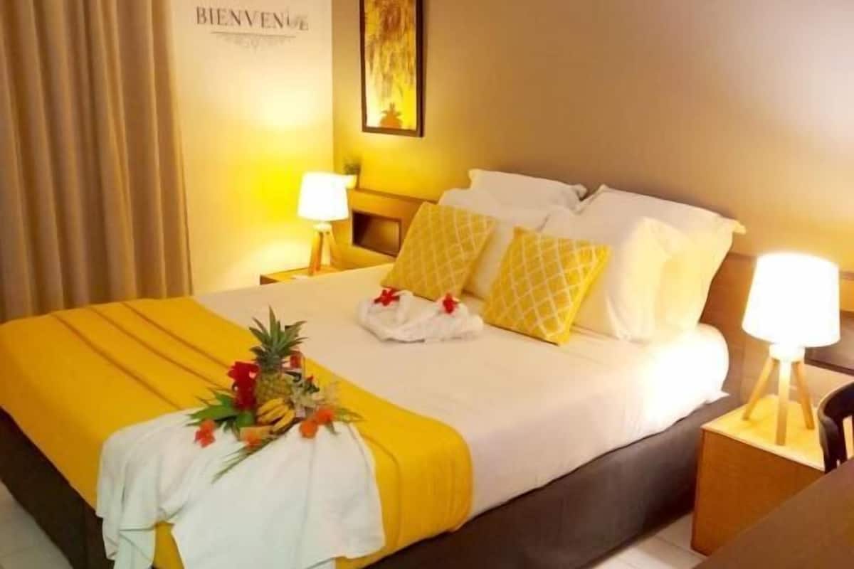 A hotel room with a bed, two bedside lamps, an air conditioning unit, and a welcome sign on the wall.