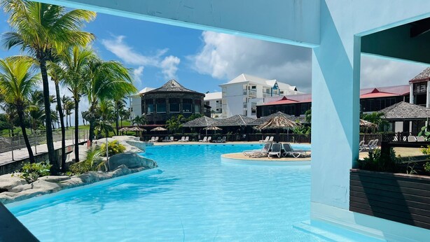 A clear blue pool with lounge chairs, palm trees, and resort buildings in the background. - Kaz ananas passion (Saint-François)