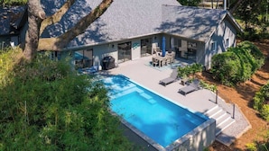 Una casa con piscina, muebles de jardín y un árbol grande.