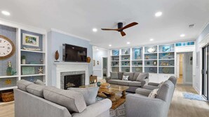 A living room with a fireplace, two grey sofas, a coffee table, and a ceiling fan. - Luxury Retreat w/ Pool Near Beach on Hilton Head (Hilton Head Island)