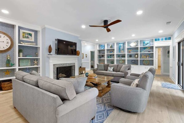 A living room with a fireplace, two grey sofas, a coffee table, and a ceiling fan.