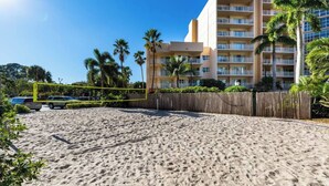 Una playa arenosa con una red de voleibol, palmeras y un edificio de hotel al fondo.